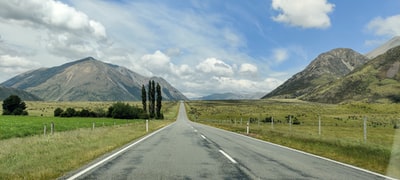 Gray cement road, near the grassy meadows and hills, in the set off of white clouds and blue sky
